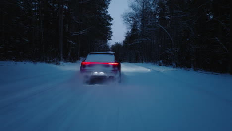 Drone-chase-shot-of-orange-Porsche-Macan-GTS-2022-model-driving-through-snowy-road-in-forest-at-dusk