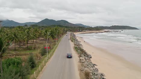 Tesla-model-3-driving-on-an-oceanside-road-along-tropical-beach-coastline