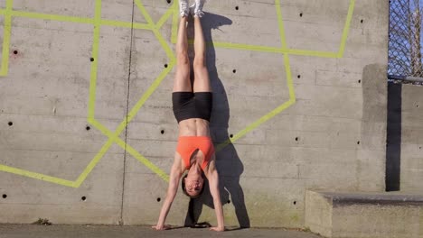 Woman-doing-handstand-against-concrete-wall-outdoors