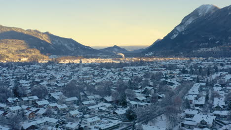 Snowy-Garmisch-Partenkirchen-town-in-shadow-of-mountains,-drone-shot
