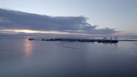 Aerial-sunset-seascape-of-Canada-Vancouver-Tsawwassen-BC-ferry-public-service-transportation,-drone-reveal-crane-port-skyline-on-calm-ocean-water