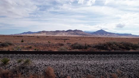 Low-drone-shot-over-a-railroad-track-with-mountains-and-desert
