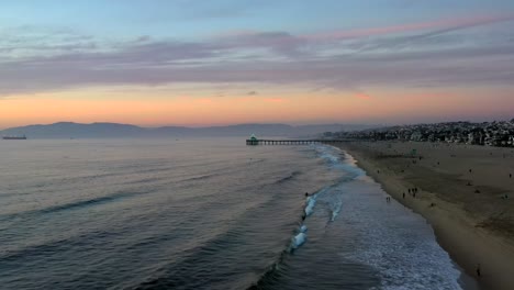 Serene-Scenery-At-Manhattan-Beach-With-Tourists-On-The-Shore-At-Sunset---aerial-drone-shot