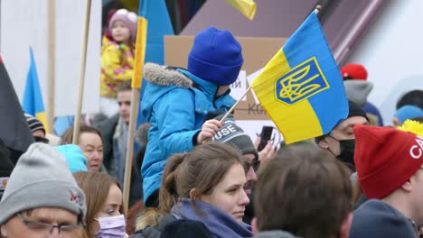 A-child-sitting-on-an-adult's-shoulder-at-an-anti-war-rally-waving-a-Ukraine-flag