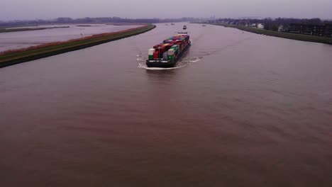 Aerial-Over-River-Noord-With-View-Of-FPS-Rijn-Ship-Carrying-Containers-Approaching-On-Cloudy-Day