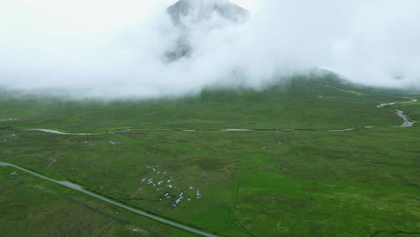 Pan-up-drone-shot-revealing-Buachaille-Etive-Mor-mountain-peak-hidden-in-white-clouds-in-Scottish-countryside