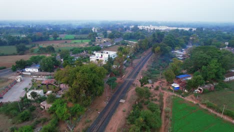 Aerial-drone-shot-traveling-upwards-of-railway-tracks,-a-highway,-and-harvest-fields-around-the-city-of-Gujarat,-Vadodara,-India