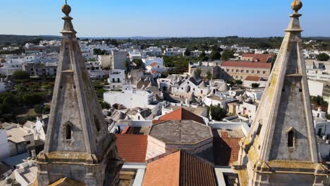 Aerial-drone-shot-fly-back-between-two-towers-of-a-cathedral-in-Alberobello,-Italy