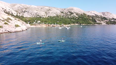 Tourists-supping-at-Krk-Island,-Croatia---Aerial-Drone-View-of-the-Coast-with-Boats,-Beach,-Mountains-and-Campsite