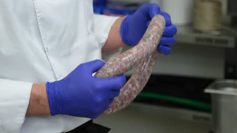 Chef-hands-close-up-in-blue-gloves-holding-fresh-meat-sausage-in-professional-restaurant-kitchen,-food-preparation