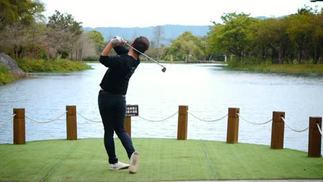 Asian-man-swings-golf-club-and-hits-golf-ball-into-a-beautiful-lake-with-beautiful-forest-view