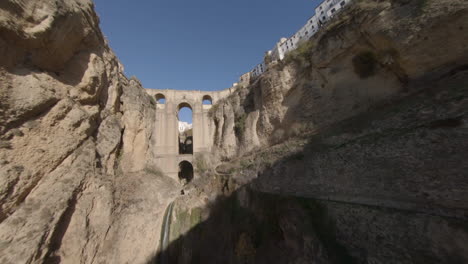Slow-aerial-flight-up-deep-gorge-toward-medieval-arch-bridge-in-Spain
