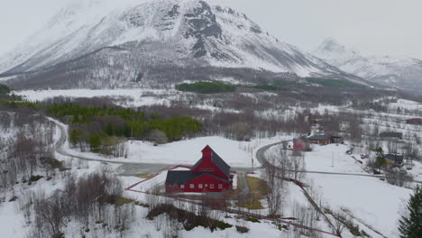 Iglesia-Kaafjord-Al-Pie-De-Una-Montaña-Cubierta-De-Nieve-En-Medio-Del-Invierno-En-Olddalen-Noruega---Toma-Aérea-En-órbita