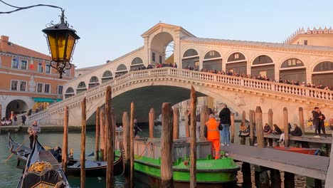 Brücke-Ponte-Di-Rialto-Und-Gondoliere-Mit-Touristen-Auf-Abfahrt-In-Der-Gondel-Bei-Sonnenuntergang,-Venedig-In-Italien
