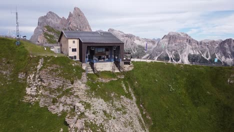 Seceda-at-Val-Gardena,-Urtijei,-South-Tyrol,-Italian-Alps,-Dolomites,-Italy---Aerial-Drone-View-of-the-Cable-Car-Station,-Green-Valley-and-Mountain-Peak