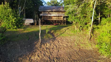 Aerial-view-moving-forward-shot,-a-wooden-hut-on-the-shore-of-the-amazon-river-in-Colombia,-tall-tree-and-bright-sunny-day-in-the-background