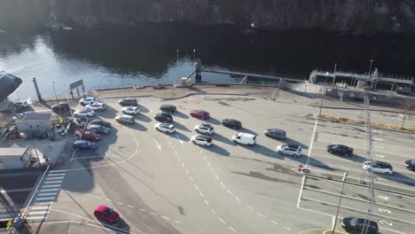 Long-line-of-cars-driving-onboard-hybrid-powered-Torghatten-ferry-from-Halhjem-ferry-pier---Ascending-aerial-with-tilt-down-along-Norway-coastal-road-E39