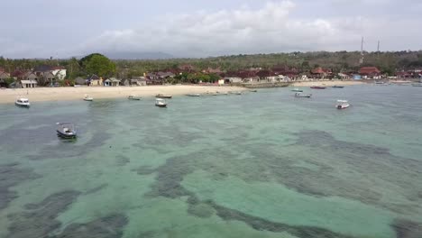 Dramatic-fast-aerial-view-flight-fly-forwards-drone-footage-over-the-reef-over-crystal-clear-turquoise-water,-boats-to-tropical-beach-Bali-at-Mushroom-Bay