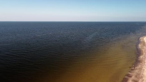 Aerial-high-altitude-view-of-sea-waves-crashing-into-the-beach-with-white-sand-on-a-sunny-spring-day,-Baltic-sea,-Pape-beach,-Latvia,-wide-angle-drone-shot-moving-forward