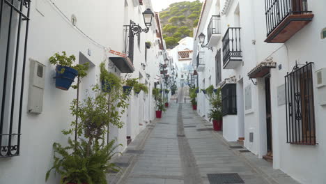 Narrow-street-with-white-facade-houses-in-spanish-town-Mijas,-pan-shot