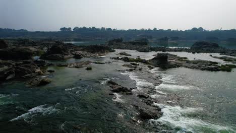 Vadodara-,-Gujarat-,-India---:-Aerial-forwarding-shot-over-Narmada-river-water-flowing-through-rocky-terrain-in-Vadodara-region,-Gujrat,-India-at-bright-sunny-daytime