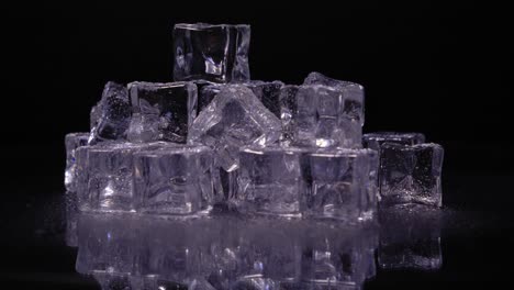 Pile-of-ice-cubes-with-a-purple-tint-rotating-against-a-black-background,-horizontal-static-studio-shot