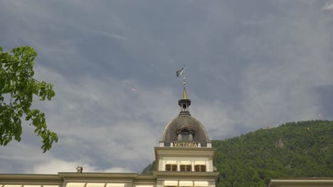 Person,-Die-Hinter-Dem-Luxuriösen-Victoria-Jungfrau-Hotel-Dome,-Alpen-Im-Hintergrund,-Interlanken,-Schweiz-Gleitschirmfliegt
