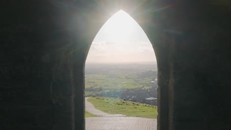 Dolly-shot-from-inside-a-gothic-church-through-doorway-to-beautiful-green-landscape-with-nice-sunlight