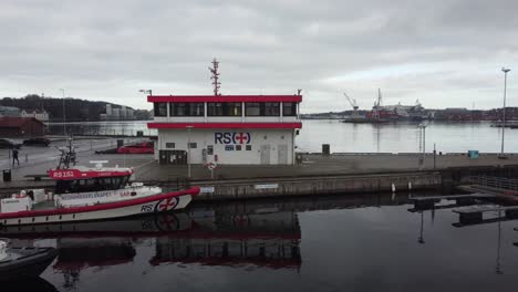Gebäude-Des-Seenotrettungsunternehmens-Redningsselskapet-In-Stavanger,-Norwegen---Annäherung-Aus-Der-Luft-An-Ein-Gebäude-Mit-Fjord-Im-Hintergrund-Und-Rettungsbooten-Davor