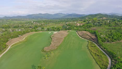 Aerial-backwards-shot-of-large-Golf-CLub-with-grass-fields-surrounded-by-mountains-on-Dominican-Republic-Island