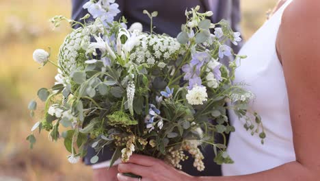 Close-Up-of-Bride-in-Her-Wedding-Dress-Holding-Large-Wildflower-Wedding-Bouquet-in-Her-Hands-in-Wedding-Dress-Outdoors-with-Groom-1080p-60fps