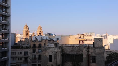 Panoramic-sunset-view-of-Our-Lady-of-the-Mount-Carmel-Church-and-city-rooftops-in-Gzira,-Malta-on-clear-summer-evening-with-high-rise-building-in-foreground