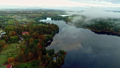 Drone-backward-moving-clip-of-water-lake-in-the-surrounded-by-trees-alongside-a-small-town-on-a-cloudy-day