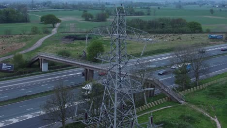 Speeding-traffic-passing-pylon-electricity-tower-on-M62-motorway-aerial-view-close-up-orbit-left