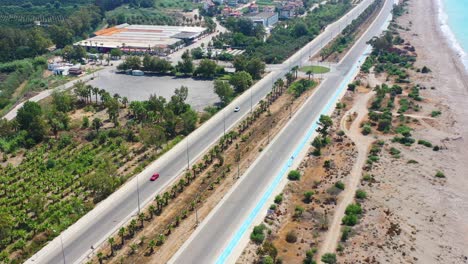 Aerial-view-of-an-empty-coastal-highway-road-in-Finike-Turkey-on-a-sunny-summer-day-with-a-sandy-beach-and-palm-trees