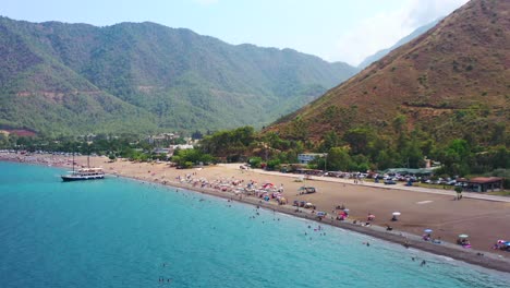 aerial-drone-reveling-the-blue-Mediterranean-coastline-of-Adrasan-Beach-full-of-tourists-and-a-dry-mountain-landscape-on-a-hot-summer-day-in-Turkey
