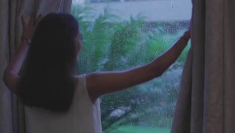 Close-up-shot-of-woman-removing-curtain-to-see-rain-from-window-in-Diu-city-of-India