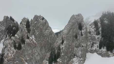 Drone-Volando-Entre-Picos-De-Montañas-En-Una-Espesa-Niebla-Y-Revelando-Un-Hermoso-Valle-Cubierto-De-Nieve