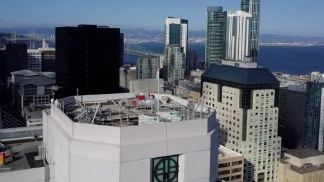 Aerial-view-towards-a-rainbow-flag-on-top-of-a-building-in-downtown-San-Francisco,-USA---tilt,-drone-shot