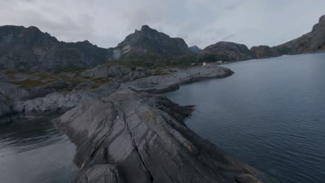 Flying-over-rocks-at-shore-of-Nusfjord,-Lofoten-looking-at-Nusfjord-and-mountains-in-the-background-in-slowmotion
