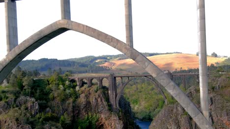 Drone-Flying-Underneath-The-New-Ulla-Viaduct-With-Old-Gundian-Bridge-In-Background-In-Galicia