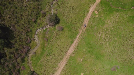 Aerial-top-down-shot-of-buggy-car-driving-on-rural-sandy-path-in-nature-of-Spain---Surrounded-by-green-forest-trees-during-sunny-day