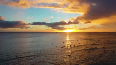 Línea-De-Surfistas-Atrapando-Olas-Al-Atardecer-En-La-Famosa-Playa-De-Waikiki,-Patrulla-Al-Amanecer-Con-Turistas-Y-Olas-En-Honolulu,-Hawaii
