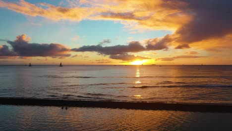 Goldene-Stunde-Sonnenaufgang-über-Dem-Ozean-In-Waikiki-Beach,-Hawaii,-Während-Wellen-Mit-Segelbooten-Und-Menschen-Gegen-Die-Bruchmauer-Schlagen