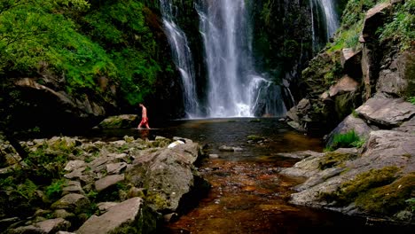 View-Of-Caucasian-Male-Wearing-Red-Shorts-Wading-Through-Water-At-Base-Of-Fervenza-do-Toxa-Waterfalls