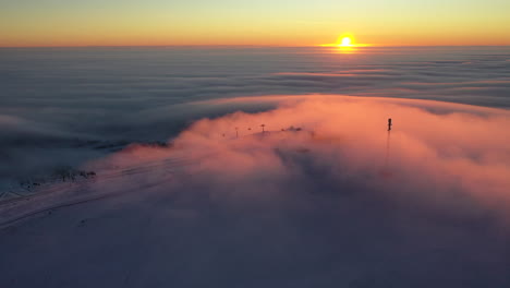 Sunrise-above-clouds-turning-them-into-orange-at-the-top-of-a-ski-resort