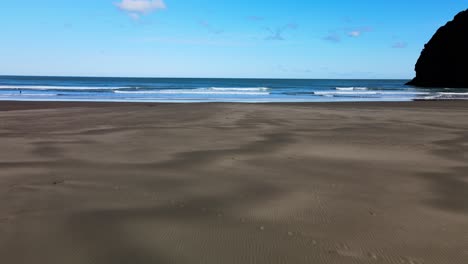 Flying-across-the-textures-of-Piha-black-sand-beach-and-into-the-famous-surf-break