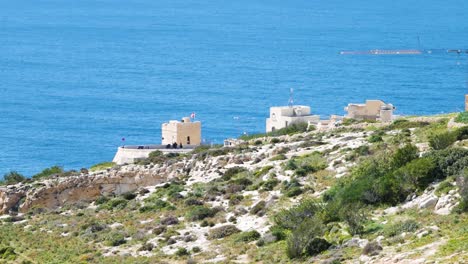 White-coastal-buildings-and-blue-ocean-water-near-Malta-island,-static-distance-view