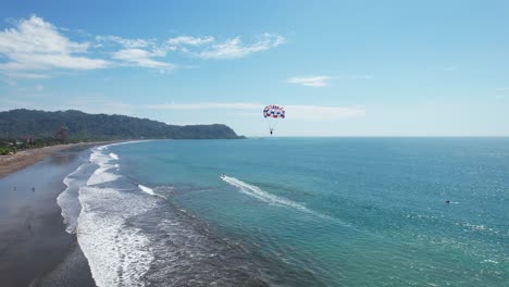 Aerial-images-of-the-beach-on-a-sunny-day,-following-water-parachute,-Aerial-drone-images,-Beach-Jaco,-Puntarenas,-Costa-Rica,-Dolly-Inn,-Tracing