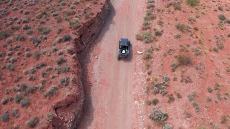 Overhead-drone-shot-of-off-road-vehicle-driving-down-a-dirt-road-in-the-desert